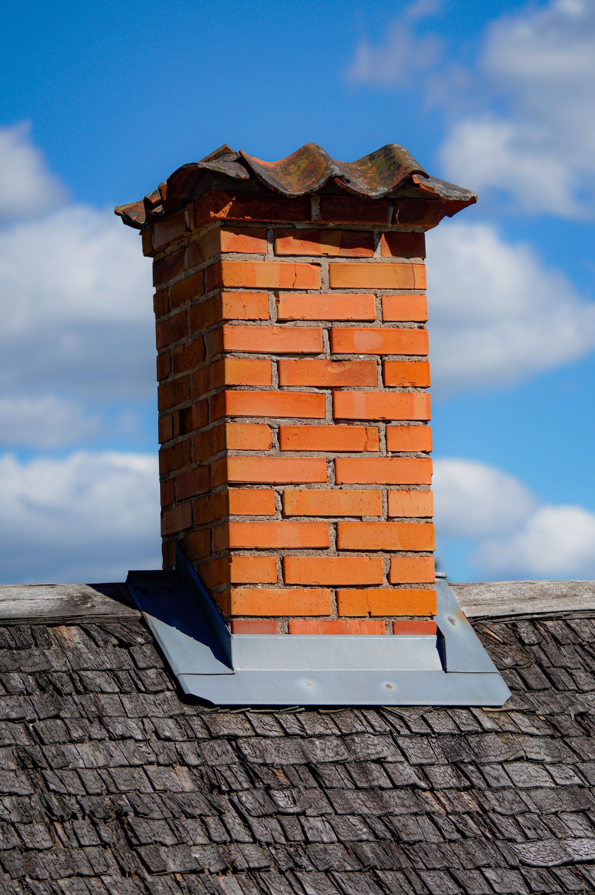 A brick chimney and the metal flashing surrounding its base