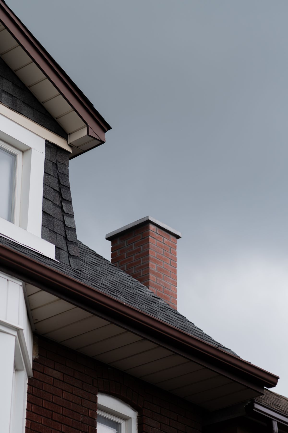A chimney and gutter where two roof planes meet beside a wall